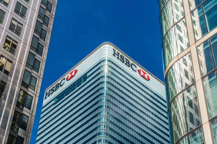 Skyscraper with HSBC sign and logo, amid other skyscrapers, blue sky.