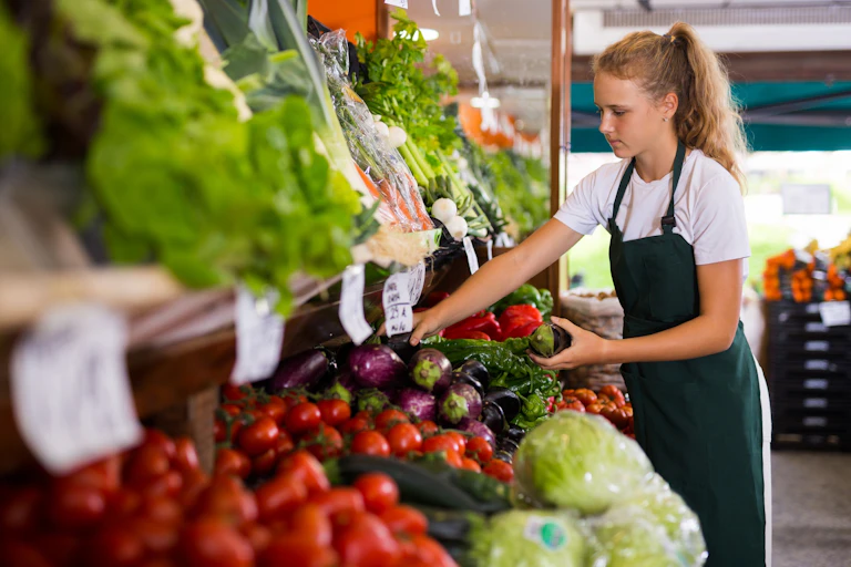 Adolescente con un mandil de trabajo coloca las verduras en un puesto de alimentos.