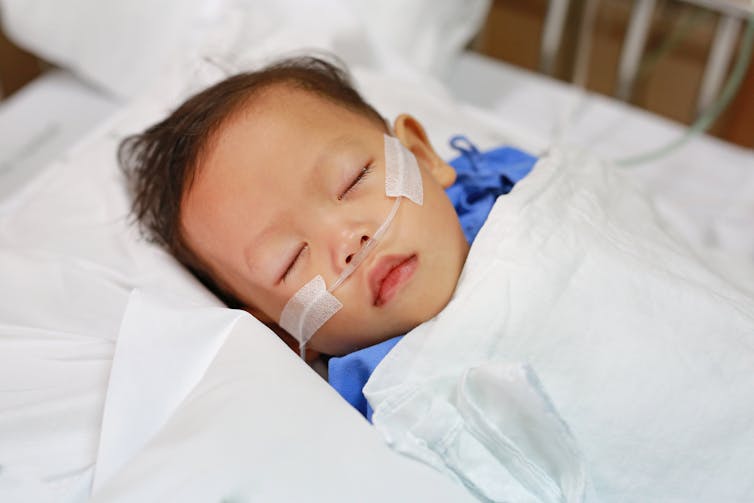 A small boy with a breathing tube sleeps in a hospital bed.