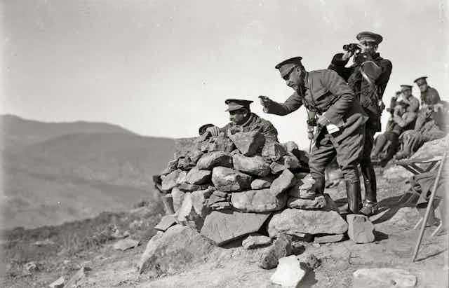 Soldados sobre unas rocas señalan y miran a lo lejos.