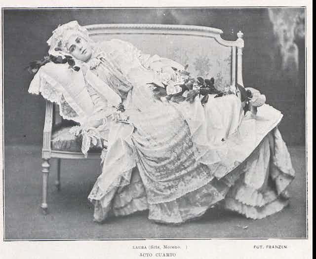 Una mujer vestida de época se recuesta seria en un sofá.