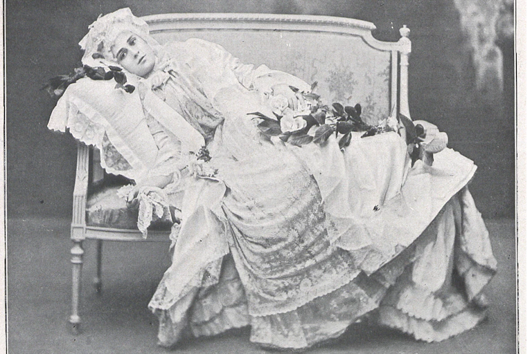 Una mujer vestida de época se recuesta seria en un sofá.