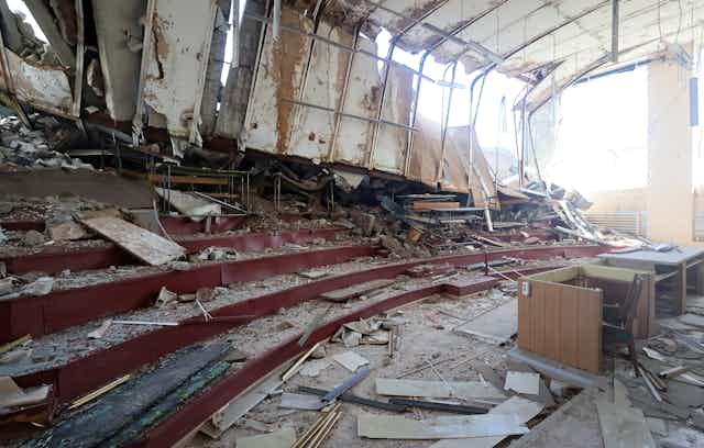 A destroyed classroom with a desk in the front of bleacher seats.