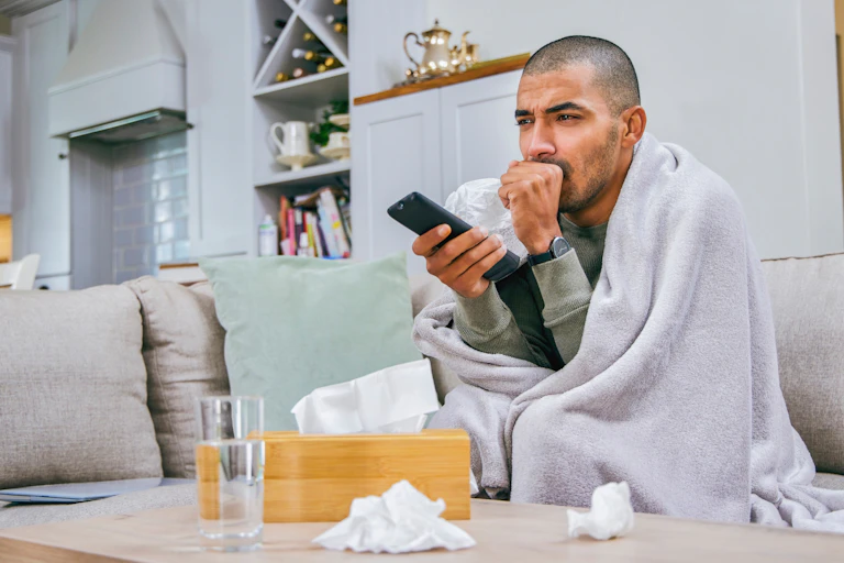 A man sitting on a couch coughing.