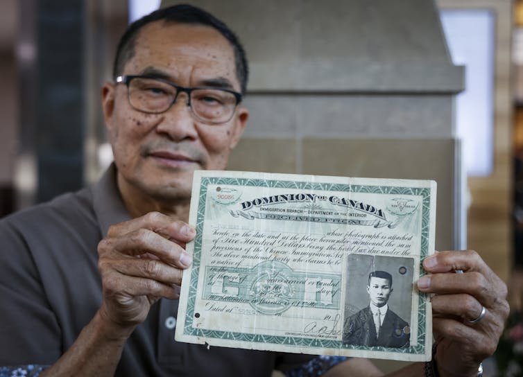 An Asian man holds a green certificate with a black and white photo of a young man in a suit and tie.