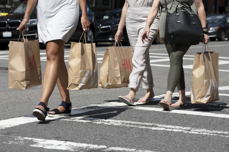 Shoulders-down view of people crossing the street holding shopping bags