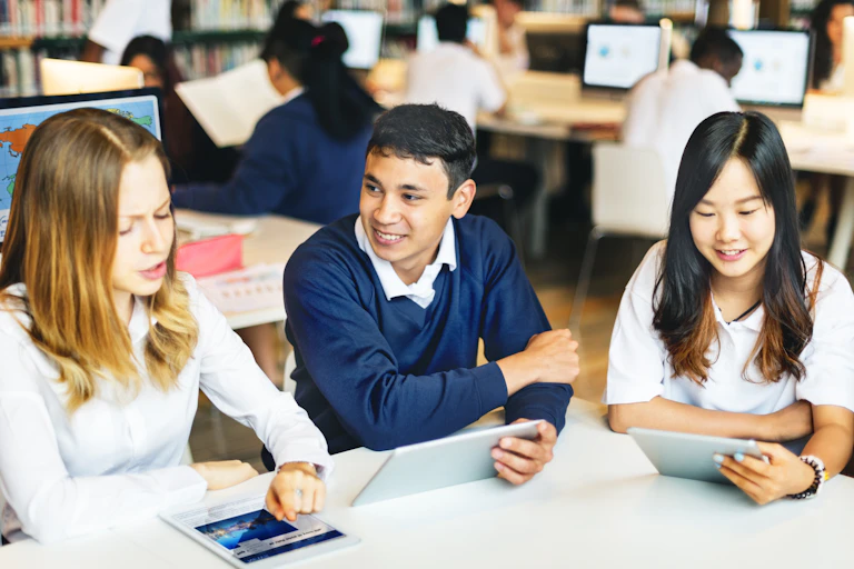 Students sit with laptops and tablets in a school library.