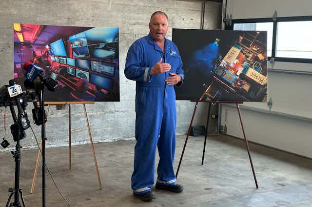 a man in blue coveralls stands in front of two easels showing images from the search