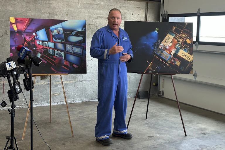 a man in blue coveralls stands in front of two easels showing images from the search