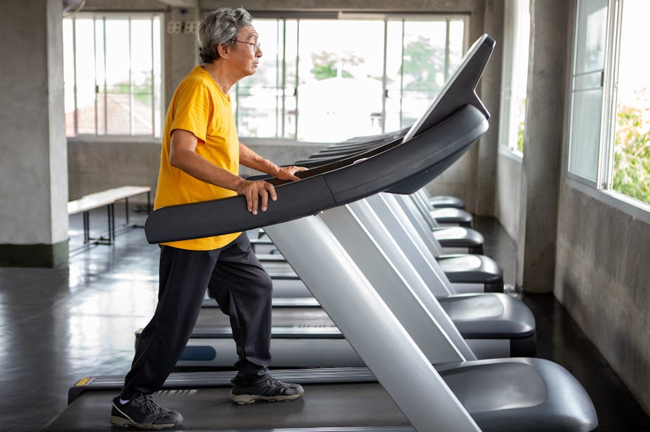 Elderly man walks on a treadmill in a gym.