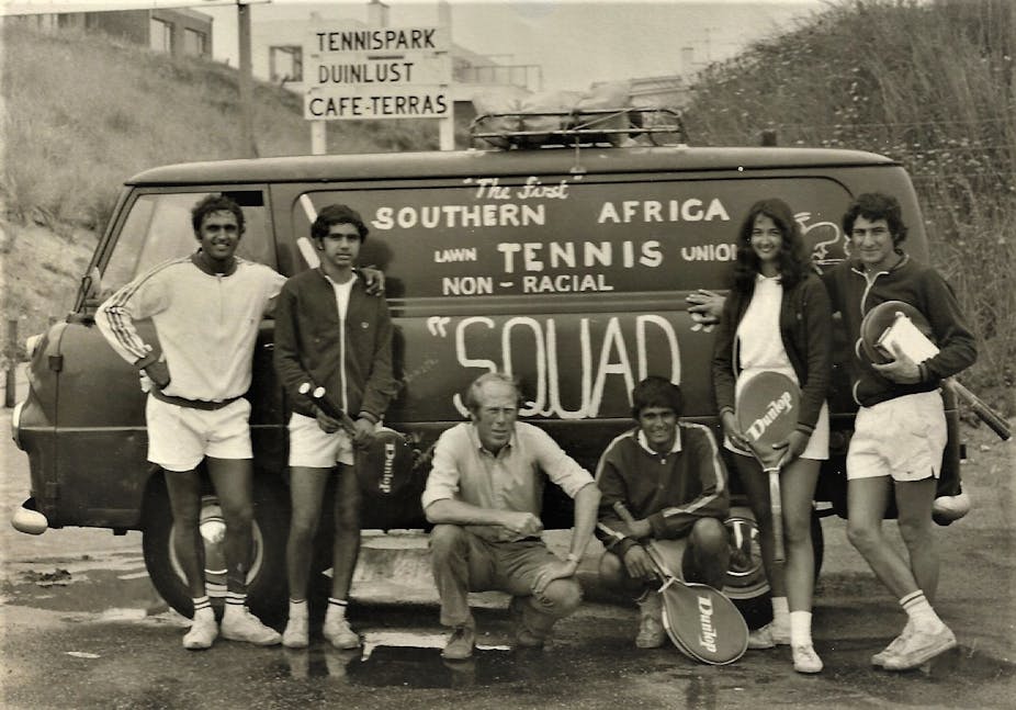 An old black and white photo of six people standing and squatting next to a motor vehicle with words painted on the side: "The first Southern African lawn tennis union non-racial squad". Some of them hold tennis rackets.