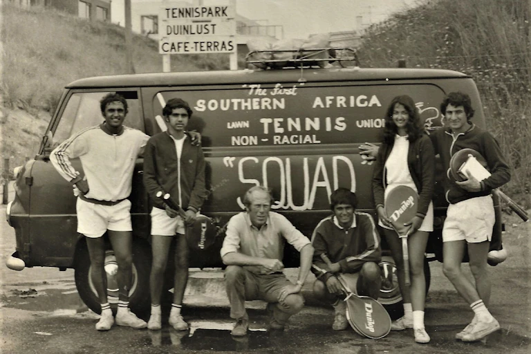 An old black and white photo of six people standing and squatting next to a motor vehicle with words painted on the side: "The first Southern African lawn tennis union non-racial squad". Some of them hold tennis rackets.