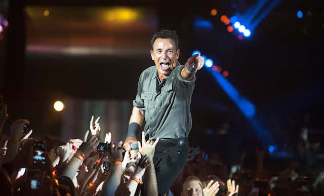 Bruce Springsteen canta entre un montón de brazos y de gente y señala con el brazo a la cámara.