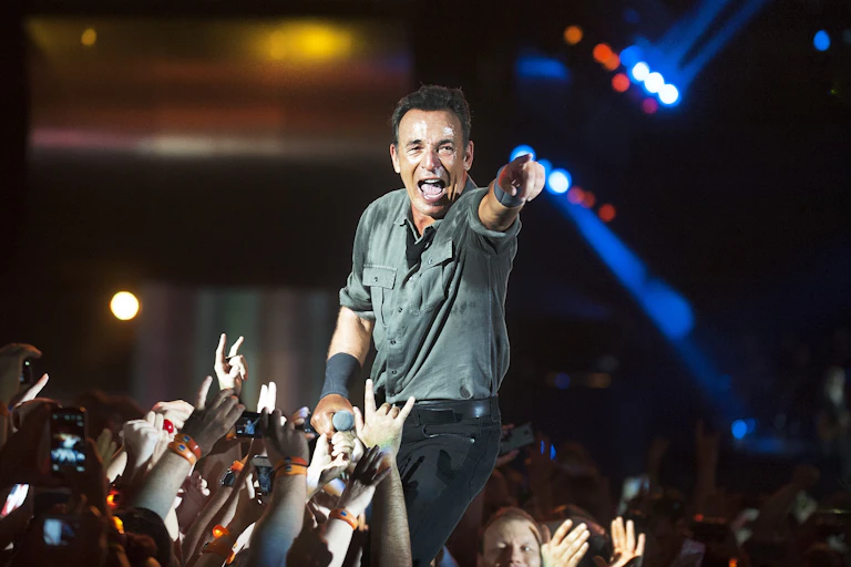 Bruce Springsteen canta entre un montón de brazos y de gente y señala con el brazo a la cámara.