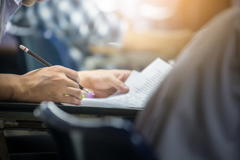 Las manos de un estudiante completan un examen a lápiz.
