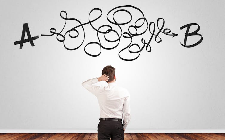 Back of man scratching head in front of white wall with