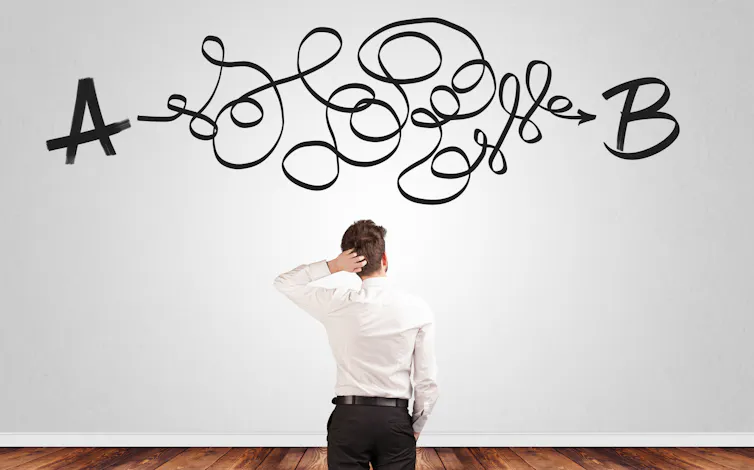 Back of man scratching head in front of white wall with