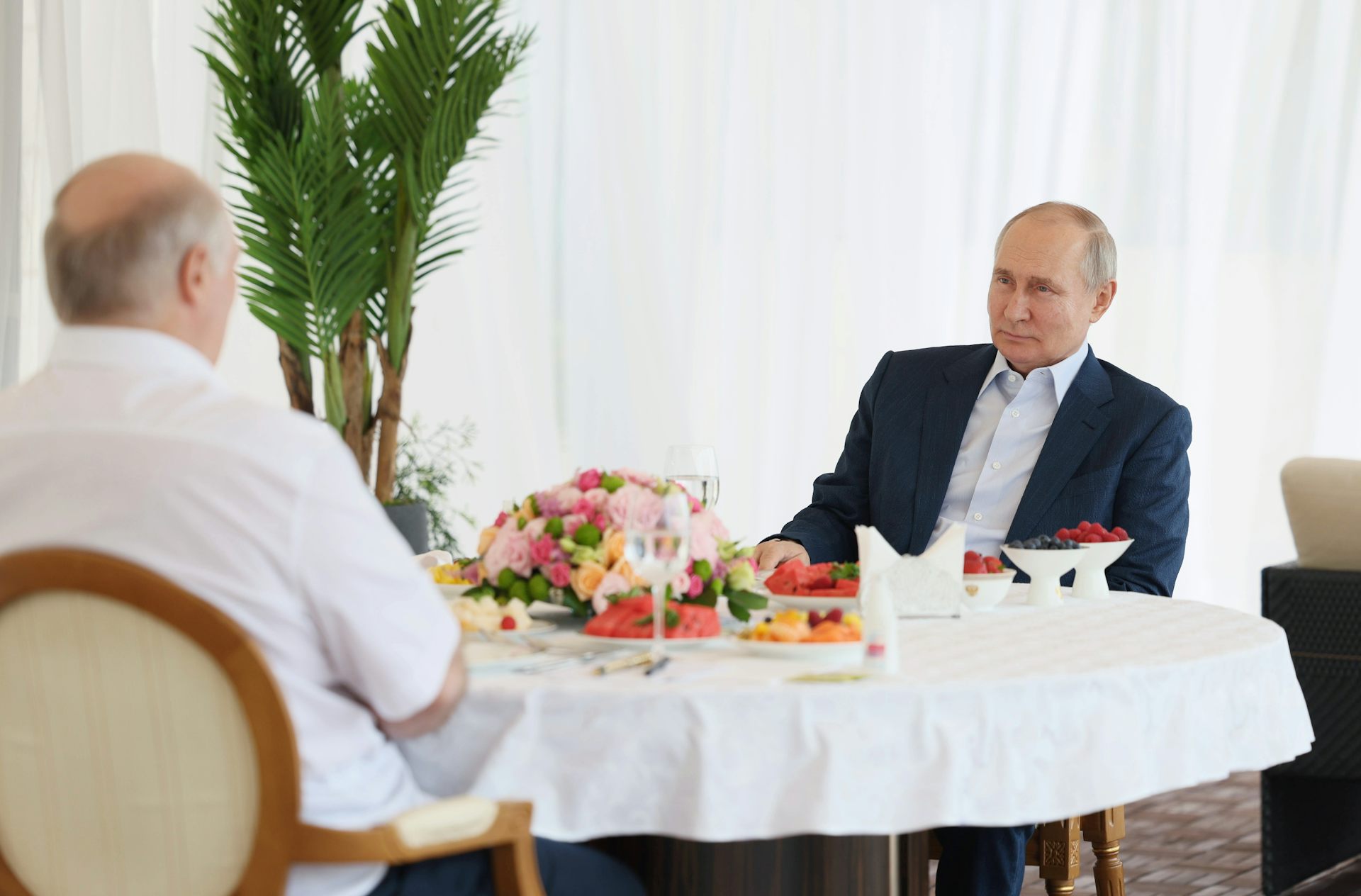 يجلس بوتين على طاولة ملطخة بالطعام مقابل رجل آخر.