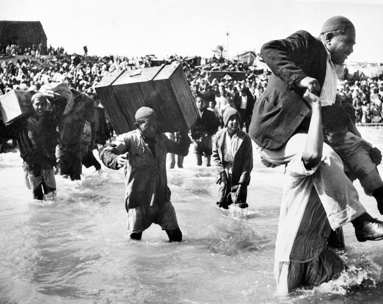 Men, women and children wading through a river.