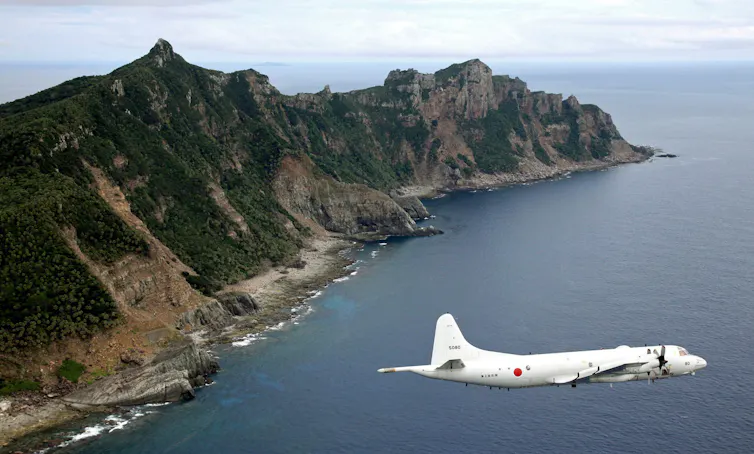 A plane flies over a hilly island.
