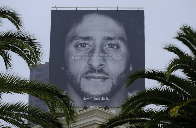 A face on a large billboard and the Nike swoosh logo framed by palm trees.