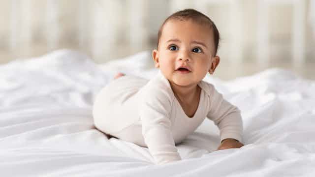 A baby wearing a bodysuit on white bedsheets.