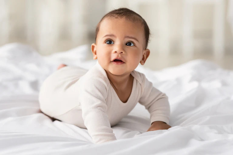 A baby wearing a bodysuit on white bedsheets.