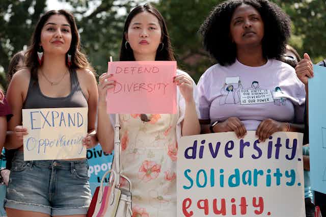 Three women of different races are holding up signs that support diversity.