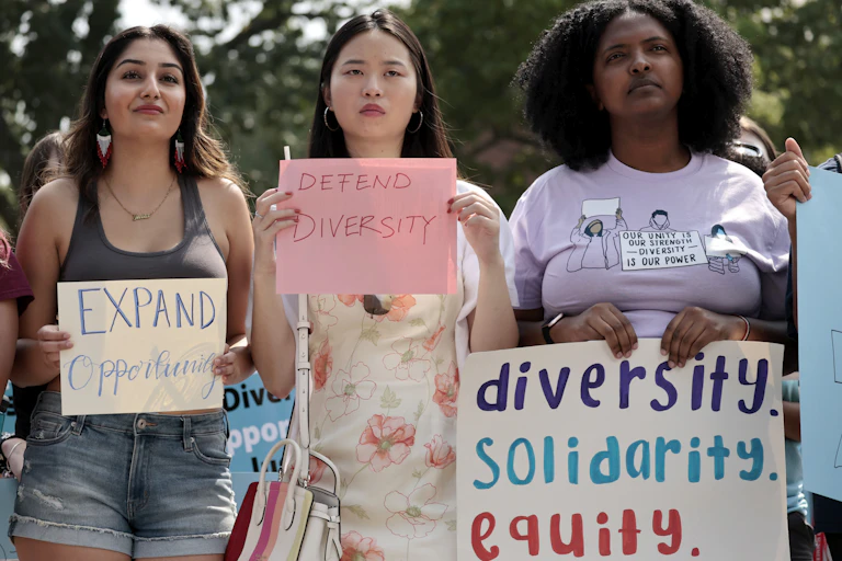 Three women of different races are holding up signs that support diversity.