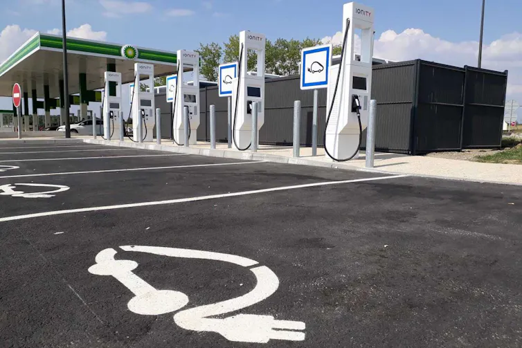 Places réservées au chargement des voitures électriques, avec les bornes en arrière plan, et un gros bloc de palissade noires derrière elles