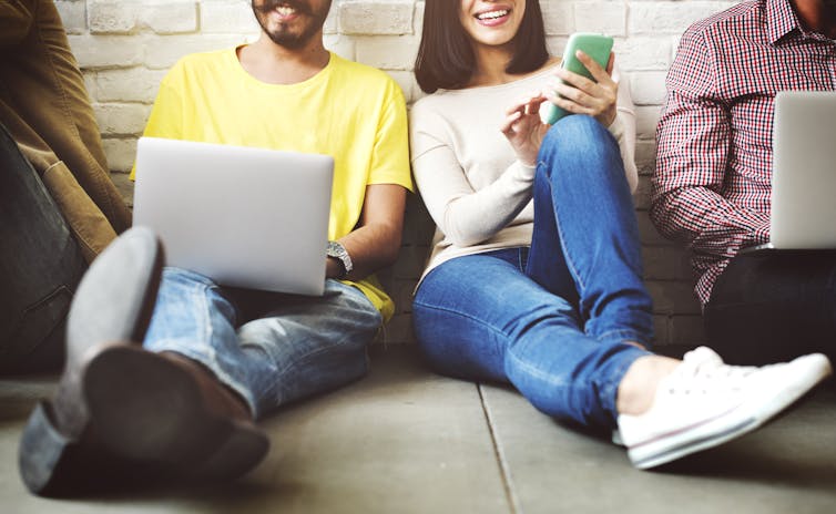 People using laptops and smartphones sitting on the ground.