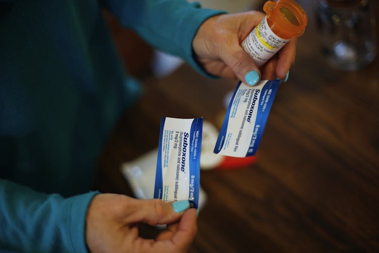Close-up photo of a woman's hands holding two small packages labeled Suboxone.