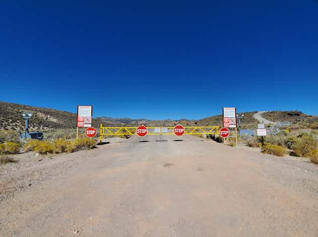 a traffic gate with four stop signs with concertina wire, floodlights and warning signs on either side on a dirt road in the desert