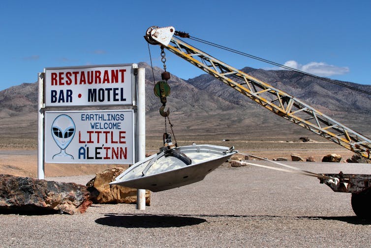 a small crane holds a disk-shaped object in front of a sign for a restaurant that includes an image of a space alien