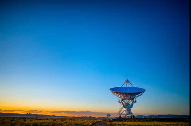 A satellite dish points towards a deep blue sky.