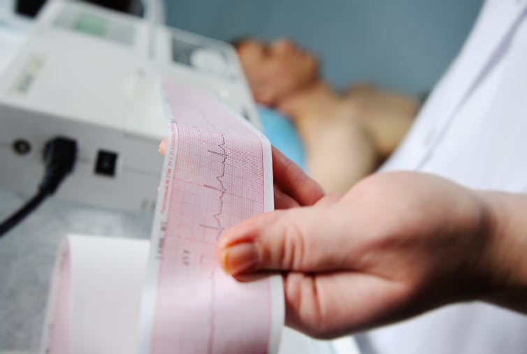 Health worker with ECG trace in hand, man lying on hospital bed in background