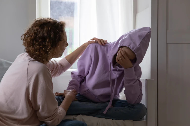 woman comforts young person with face covered