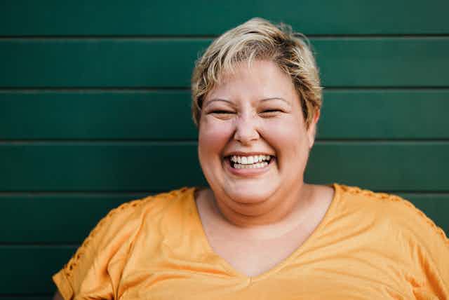 Smiling woman with obesity in yellow t-shirt against green wall