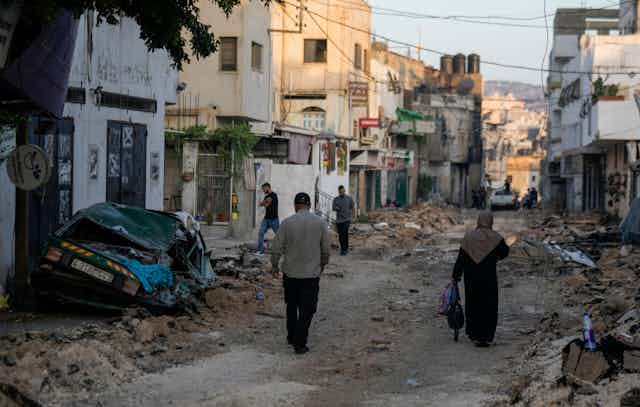 Men and women walk through the rubble of Jenin refugee camp after an Israeli attack, July 2023.