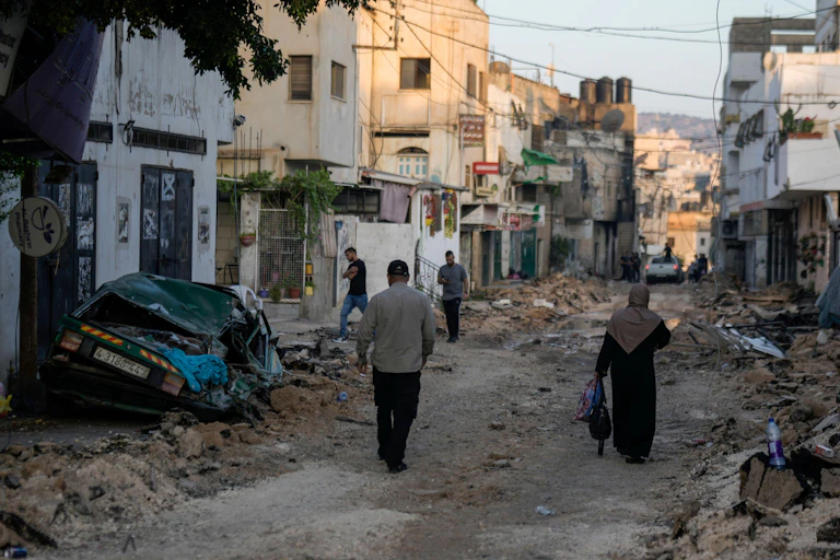 Men and women walk through the rubble of Jenin refugee camp after an Israeli attack, July 2023.