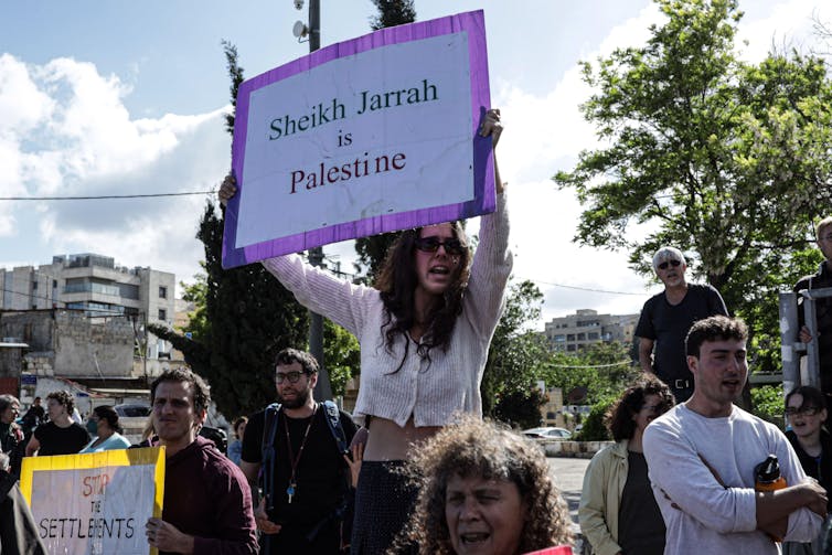 A crown of protesters with a woman holding a sign saying 'Sheikh Jarrah is Palestinian'.