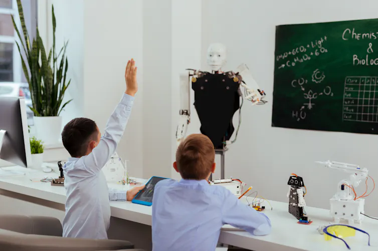 Un profesor robot da clase delante de una pizarra a dos alumnos, uno de los cuales levanta la mano.