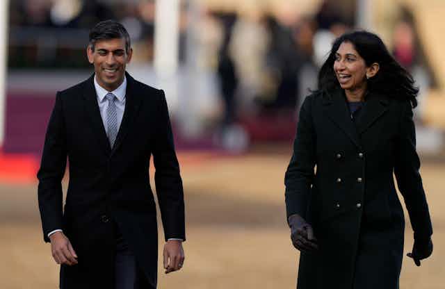 Rishi Sunak and Suella Braverman walking side by side, both smiling or laughing, in formal, black wool coats