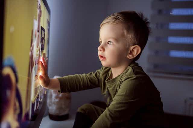 Un niño pequeño toca la pantalla de una televisión de muchas pulgadas.