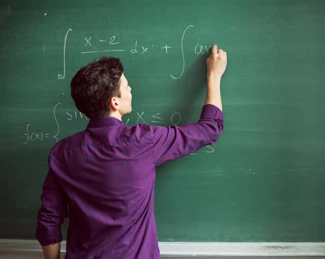 A student completing a math equation on a chalkboard.