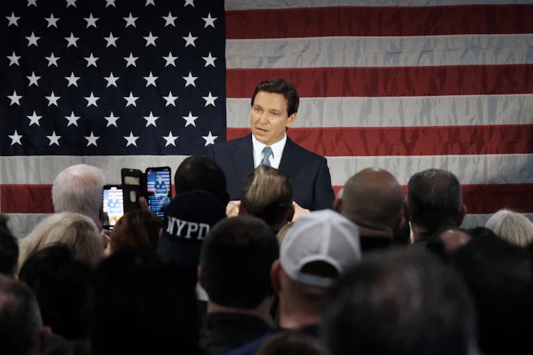 Florida Governor Ron DeSantis stands in front of American flag and speaks to crowd