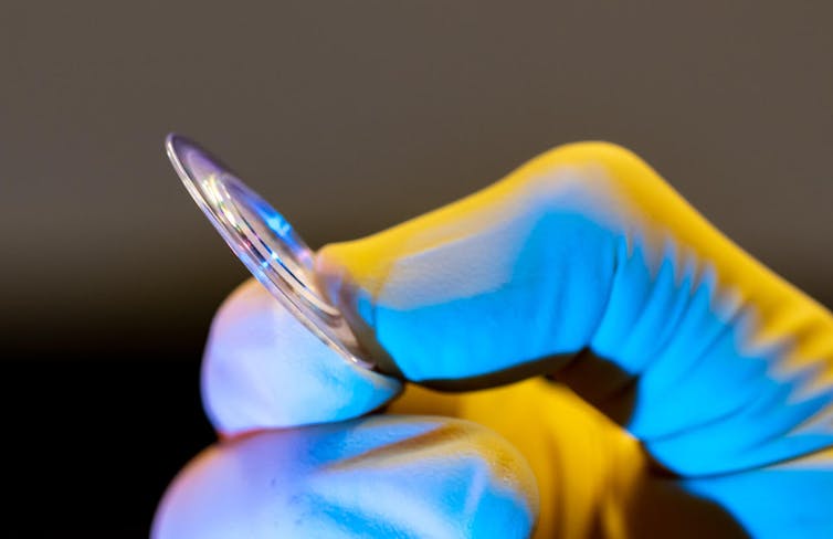 A person holding a round, thin piece of glass.