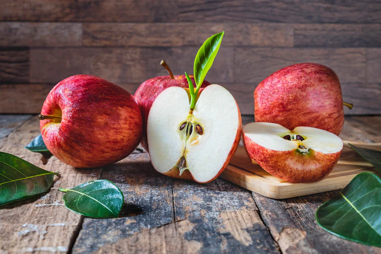 Four red apples with one cut in half lie on a wooden floor