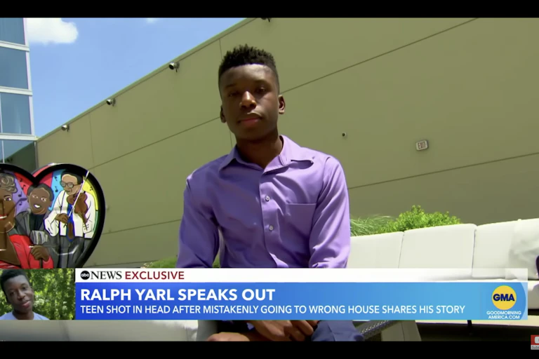 A Black teenager stands in front of a building.