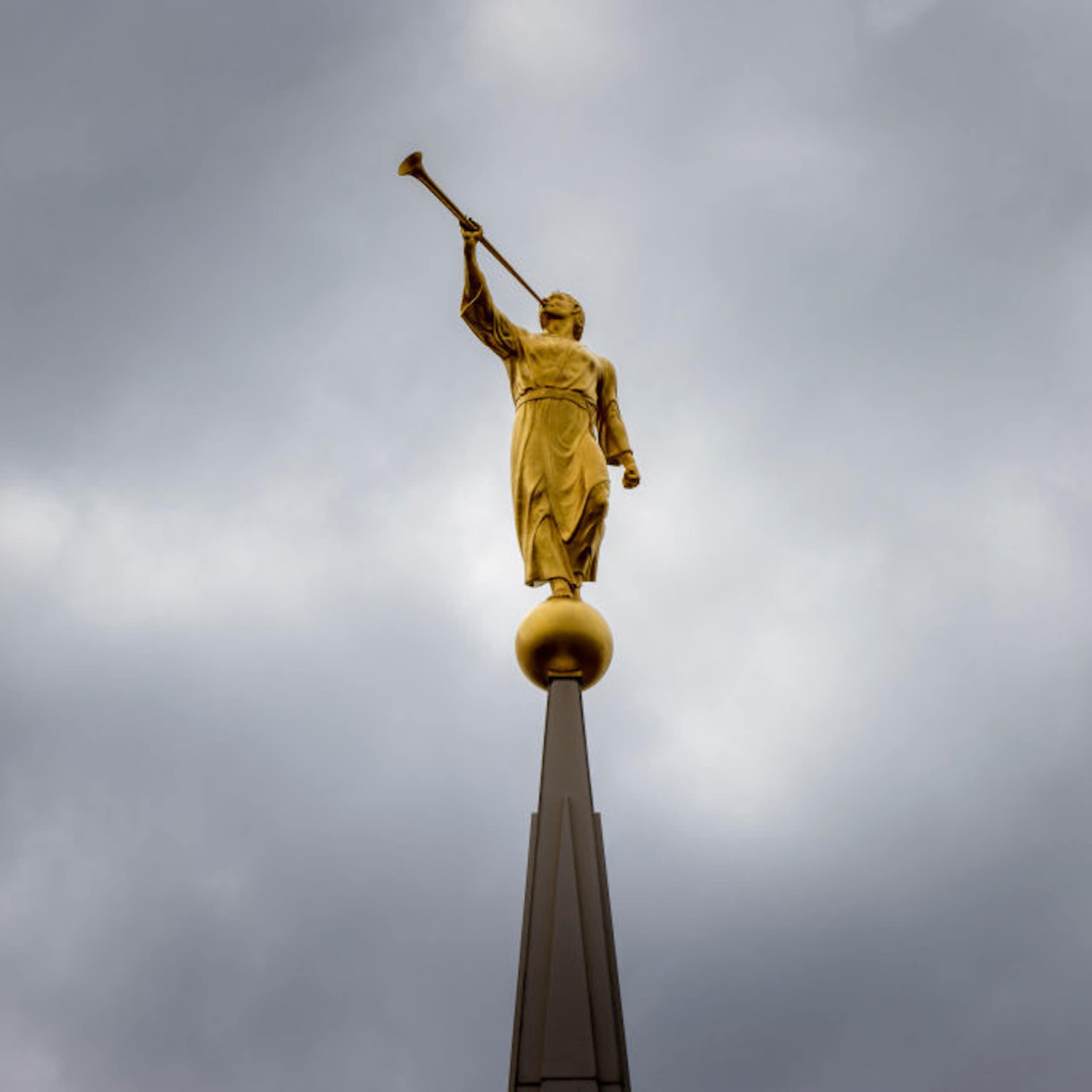 A golden statue of a man in a robe blowing a trumpet atop a steeple, seen against a gray sky.